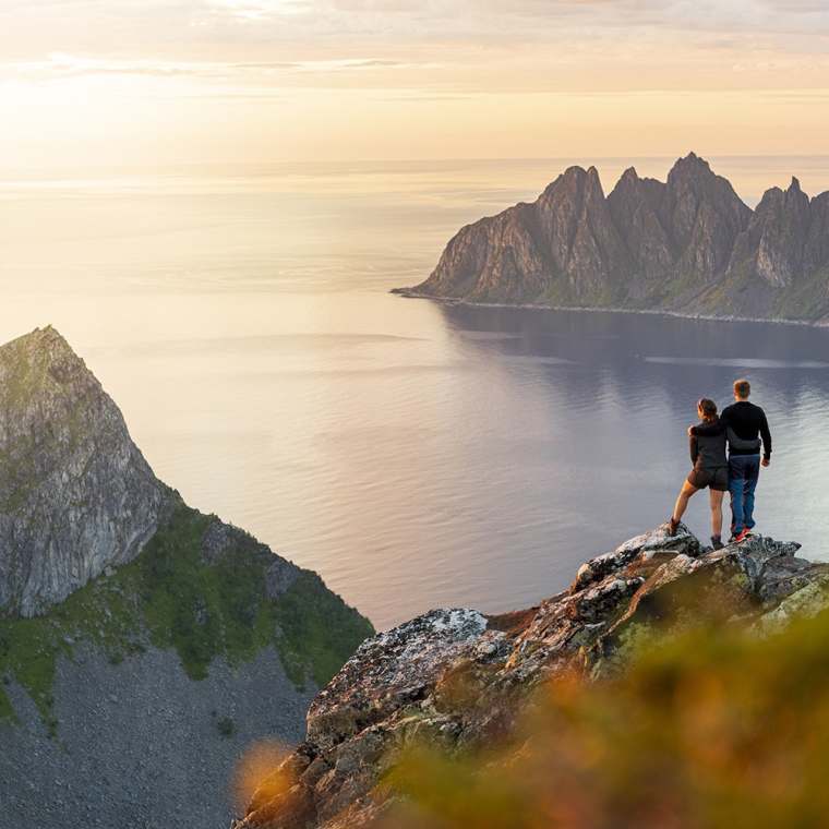 a couple standing out on the mountain peak above the Fjord Senja in Norway