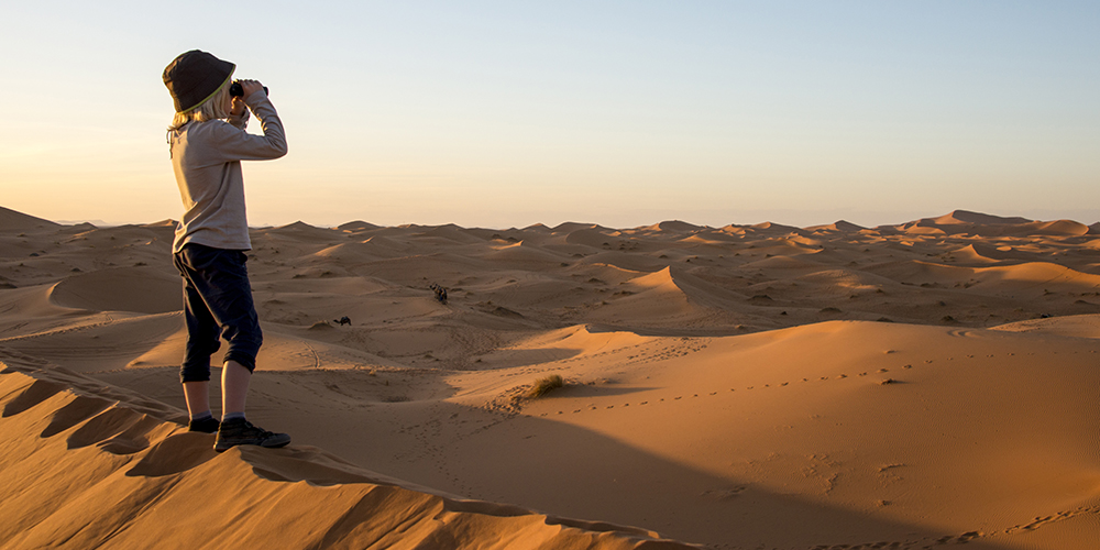 Young child standing on the dunes iwth binoculars in Morocco