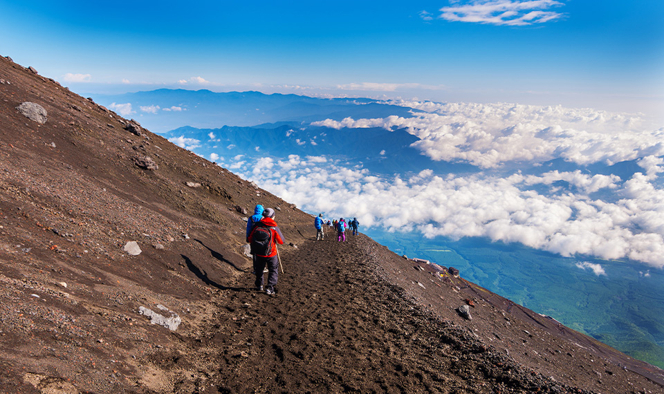 People walking along the edge of Mount Fuji above the clouds